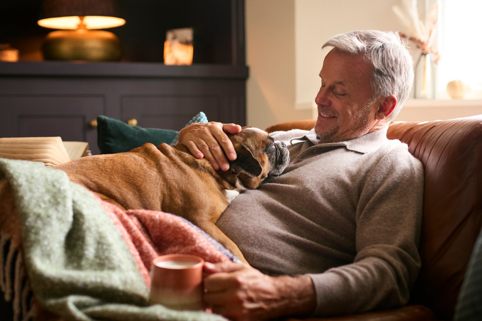 Un homme souriant caresse son chien allongé sur lui dans le canapé.